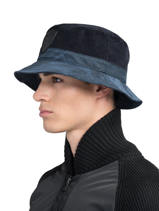 Kaia Unisex Tailored Bucket Hat in a 100% cotton corduroy and 3-ply micro denier fabrication, unstructured crown, black leather Nobis shield logo on crown front, and small flap pocket on the right side crown, in Navy + Navy