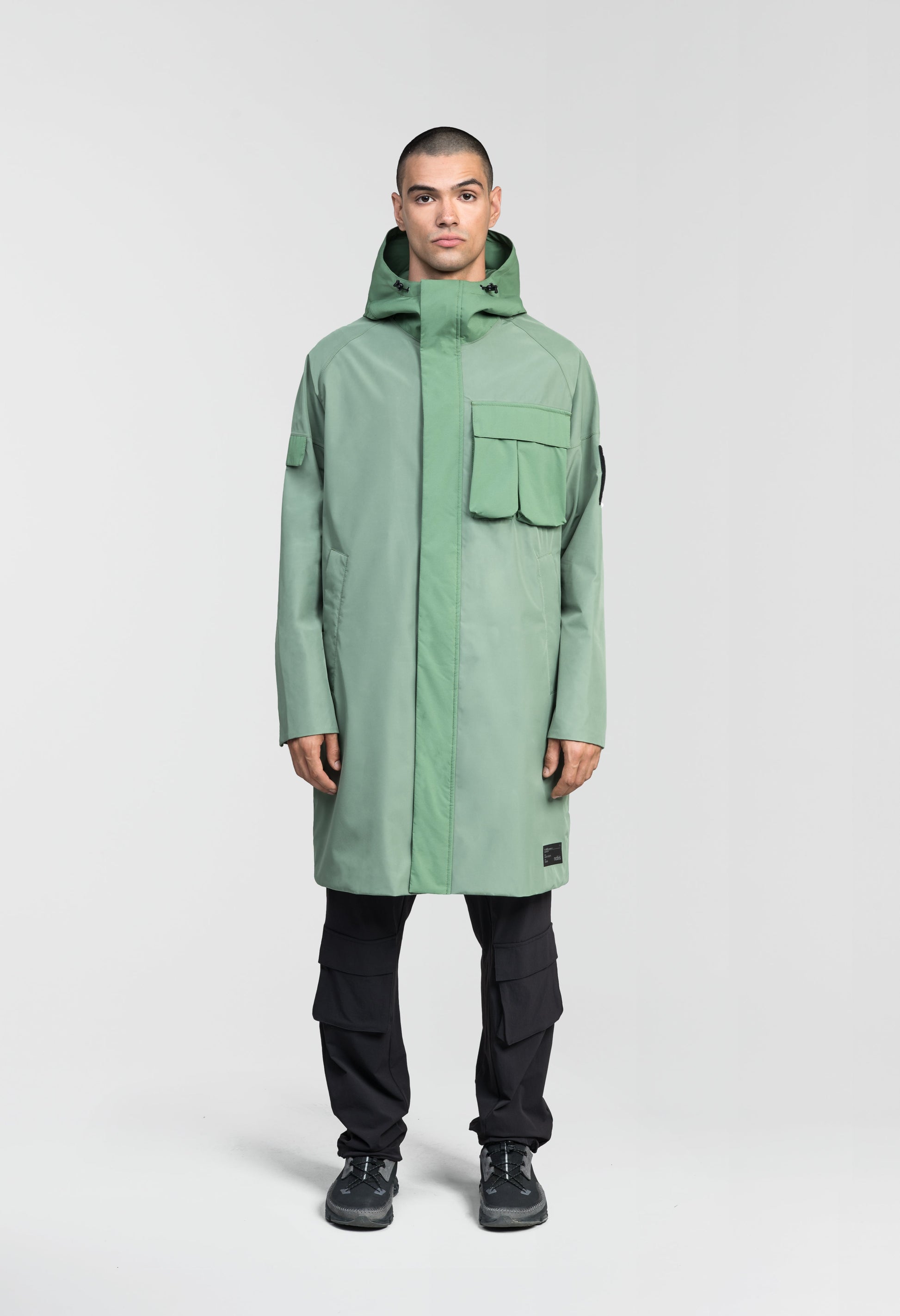 Wylder Men's Performance Rain Jacket in knee length, premium 3-ply Micro Denier and stretch ripstop fabrication, non-removable hood with reflective piping and adjustable draw cord, split utility chest pocket with magnetic flap closure, single welt pockets with magnetic closure at waist, back yoke with mesh ventilation, snap button wind flap, two-way branded zipper at centre front, telescopic sleeves with elasticized cuffs, interior draw cord at waist, in Comfrey