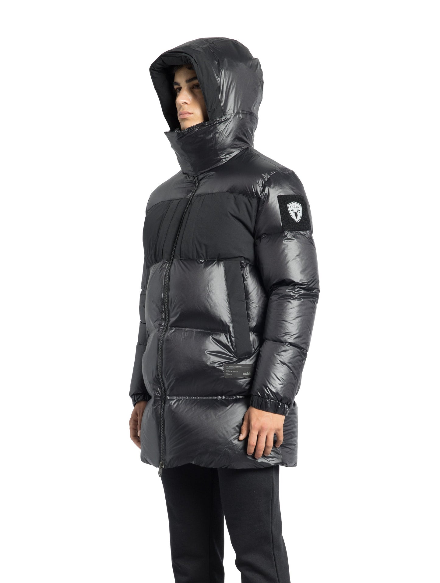 Neelix Men's Long Puffer Jacket in thigh length, premium cire technical nylon taffeta and stretch ripstop fabrication, Premium Canadian origin White Duck Down insulation, non-removable down-filled hood, two-way centre-front zipper, pit zipper vents, hidden chest zipper pockets, fleece-lined magnetic closure waist pockets, in Black